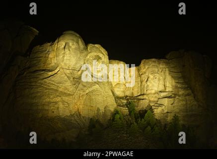 The four presidents on Mount Rushmore are illuminated with floodlights against a black sky at night Stock Photo