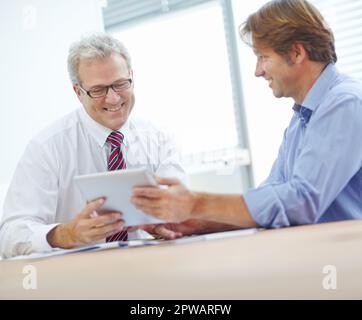 Strategies are looking positive. Two male colleagues expressing positivity and looking over the contents of a tablet. Stock Photo