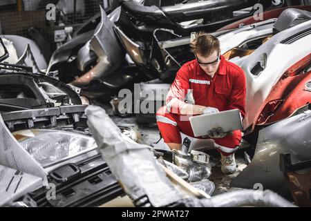 Old used car part warehouse worker checking inventory in garage. Staff worker working in recycle motor junkyard auto parts management. Stock Photo