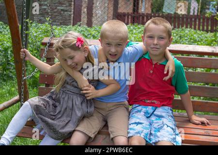 girl and two boys lay on stomach on the green grass and eat apples Stock Photo