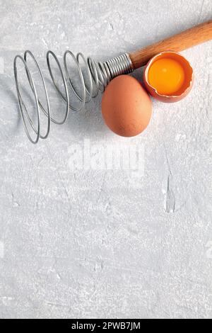 Two beige chicken eggs and a rare beater for beating. Cooking ingredients isolated on white background. Top view with copy space Stock Photo