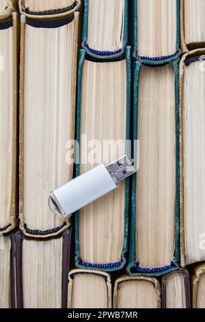 Computer usb drive on the background of a stack of old paper books. Information storage media. Top view with copy space Stock Photo