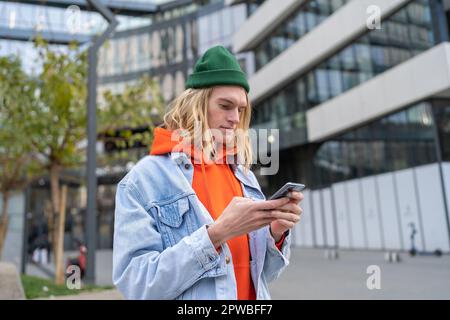 Millennial hipster guy browsing internet on mobile phone while standing on city street Stock Photo