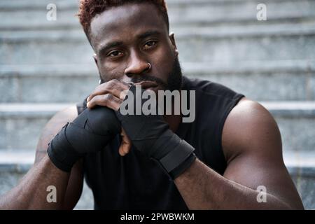 Fit confident sporty young black man boxer fighter sitting outdoors. Stock Photo
