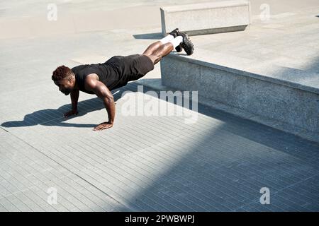 Fit sporty young black man doing push ups exercise in urban park. Stock Photo