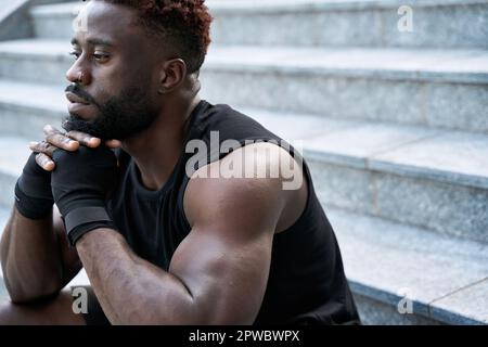 Fit confident sporty young black man boxer fighter sitting outdoors. Stock Photo