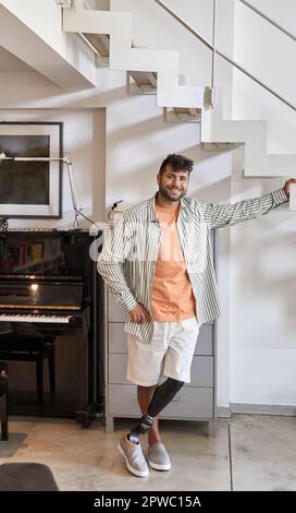 Happy young man with above knee leg prosthesis standing at home. Stock Photo
