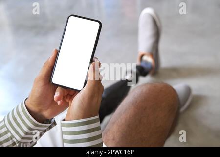 Amputee man with leg prosthesis sitting on sofa at home using phone. Stock Photo
