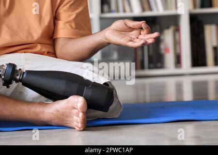 Amputee man with prosthetic leg prosthesis meditating doing yoga at home. Stock Photo