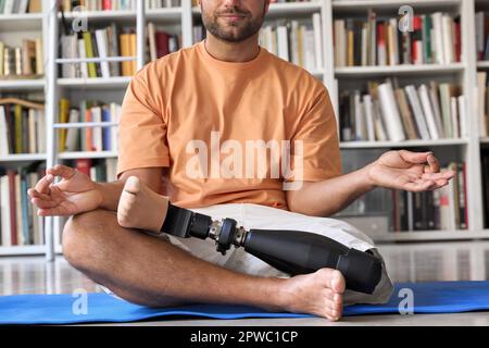 Amputee man with prosthetic leg prosthesis meditating doing yoga at home. Stock Photo