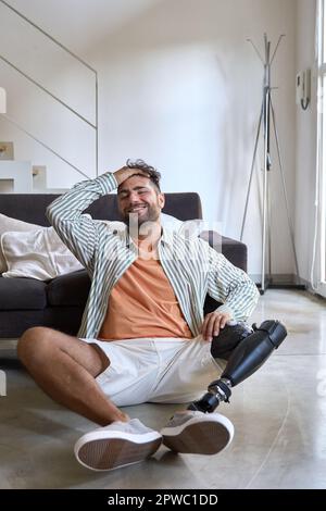 Happy relaxed amputee man with leg prosthesis sitting on floor at home. Stock Photo