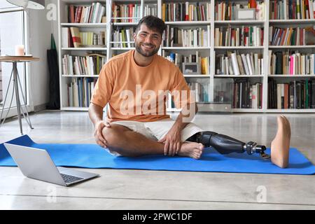 Amputee man with prosthetic leg prosthesis doing exercises at home with laptop. Stock Photo