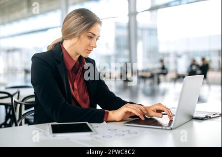 Focused busy successful caucasian woman, financial manager, executive, sitting at her desk in a modern office, working with a laptop on a important project, concentrated analyzing goals and results Stock Photo