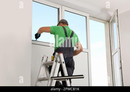 Worker on folding ladder installing window indoors Stock Photo