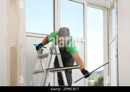 Worker on folding ladder installing window indoors Stock Photo