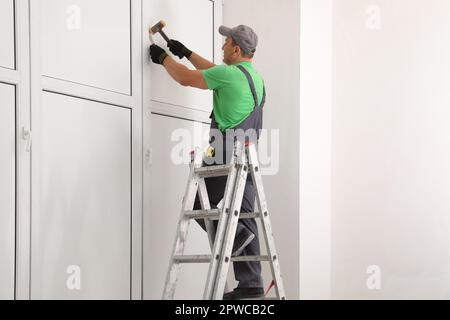 Worker on folding ladder installing window indoors Stock Photo
