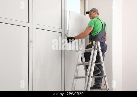 Worker on folding ladder installing window indoors Stock Photo