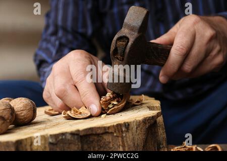 Man cracking walnuts with hammer at table, closeup Stock Photo