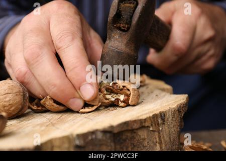 Man cracking walnuts with hammer at table, closeup Stock Photo