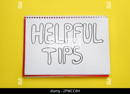 Phrase Helpful Tips in notebook on yellow background, top view Stock Photo