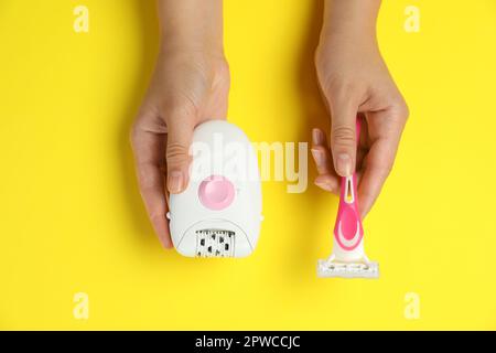 Woman holding modern epilator and razor on yellow background, top view Stock Photo
