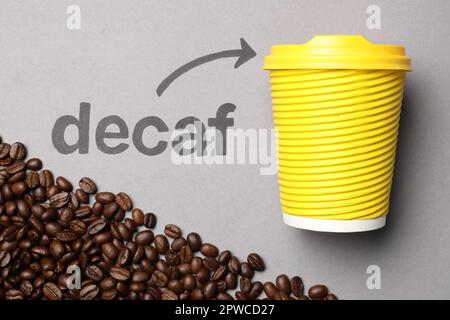 Coffee beans, word Decaf and arrow pointing at takeaway paper cup on light grey background, flat lay Stock Photo