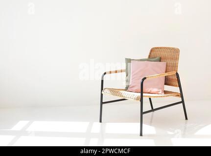 Comfortable wicker armchair with soft cushions placed near window in bright modern apartment Stock Photo