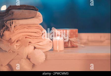 Stack of knitted plaids with gray mug and burning candle on cozy window Stock Photo