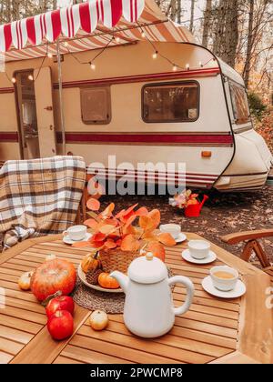Wooden chairs and table with tea set placed outside cozy retro caravan on autumn day in peaceful countryside Stock Photo