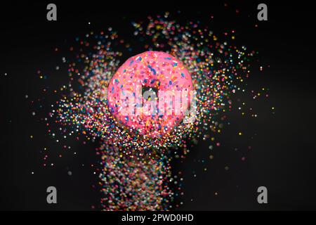 Colorful, abstract shot of delicious, sweet, pink frosted doughnut surrounded by rainbow sprinkles on matte black aesthetic background Stock Photo