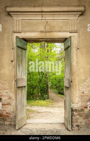 Wonderful view of a park or woods with lush green vegetation through a wooden open door and a stone wall of an ancient castle in San Sebastiano da Po Stock Photo