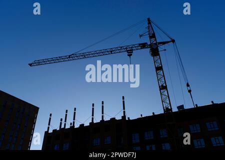 Silhouette high rise crane and building under construction against blue sky Stock Photo