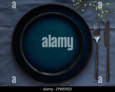 Festive table setting with flowers on blue background, flat lay. Celebration. Dark serving composition. Elegance blue tablescapes. View from above. Stock Photo