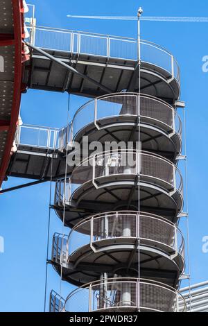 Circular iron staircase for fire escape outside a modern metal industrial building fence in the open air. Stock Photo