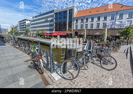 Cycles by bridge near shops, restaurants, cafes, bars and offices on Aboulevarden by River Aarhus riverside in city centre, Aarhus Denmark. Stock Photo