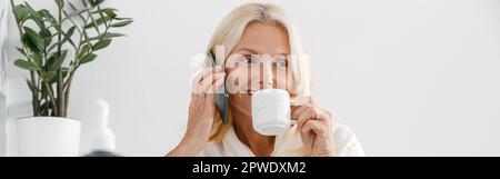 Pretty Caucasian blonde woman customer in modern light cosmetology center uses mobile phone Stock Photo