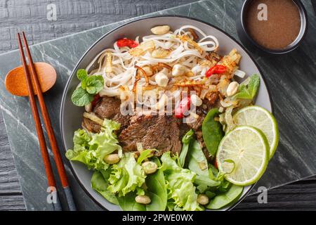 Pho Bo Tron Mixed beef noodles salad is a popular dish in Vietnamese cuisine closeup on the bowl on a wooden table. Horizontal top view from above Stock Photo