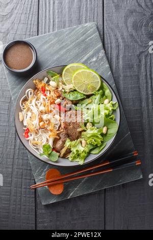 Pho tron or mixed pho is a classic Vietnamese dish a salad with meat beef, noodles and greens closeup on the plate on the wooden table. Vertical top v Stock Photo