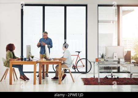 Keeping his employees on track. a mature businessman addressing two employees in the office. Stock Photo