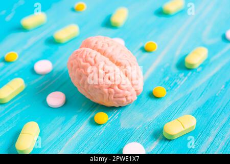 Miniature human brain model alongside scattered yellow and white pills on a blue wooden table. Brain function, medication, treatment and preserving co Stock Photo
