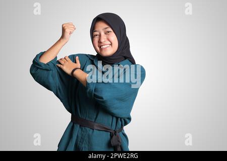 Portrait of excited Asian muslim woman with hijab showing strong biceps, demonstrating strength. Isolated image on white background Stock Photo