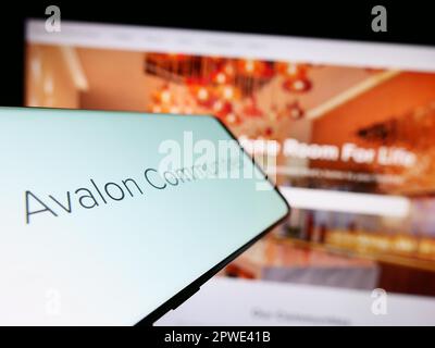Mobile phone with logo of American real estate company AvalonBay Inc. on screen in front of website. Focus on center-left of phone display. Stock Photo