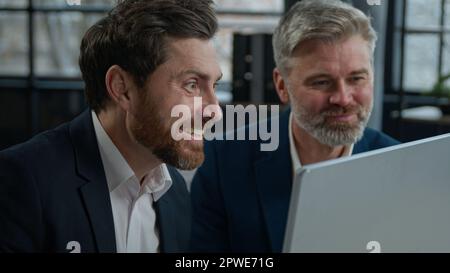 Close-up two surprised caucasian men different ages businessmen colleagues look in surprise at computer screen amazed corporate employees business Stock Photo