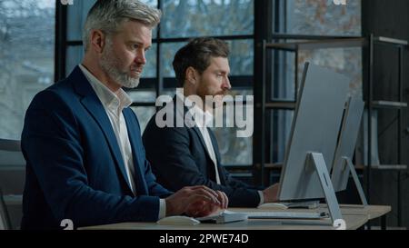 Focused professional managers working with computers on project sit in row at desk in office caucasian adult business men businessmen corporate Stock Photo