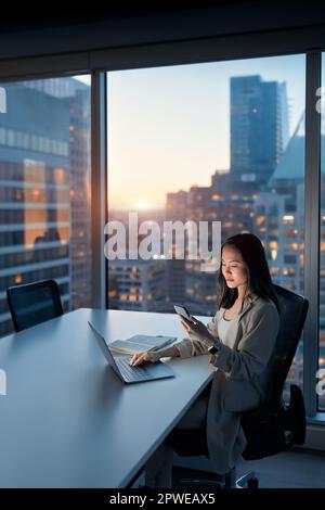 Young busy Asian business woman working using mobile at night in office. Stock Photo