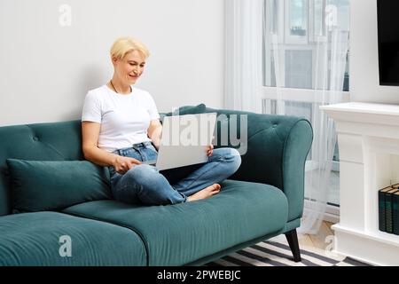 Middle aged woman chatting with friend in her new apartment online. Concept of clever ageing and adaptation to new reality. Stock Photo