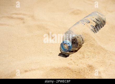 Plastic bottle on sandy beach. Empty uncapped used plastic drinking water bottles piled up with sand, dumped on the beach with copy space. Polluted ga Stock Photo