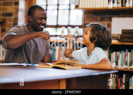 Teacher and student giving each other a high five in a library. Elementary school boy having a private lesson with his teacher. Tutoring and student s Stock Photo