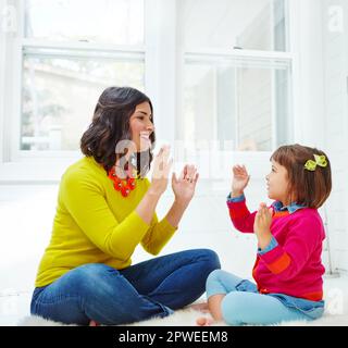 Pat a cake, pat a cake. an adorable little girl playing a clapping game with her mother at home. Stock Photo