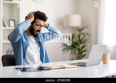 Deadline Stress. Shocked indian man looking at laptop screen and touching head Stock Photo